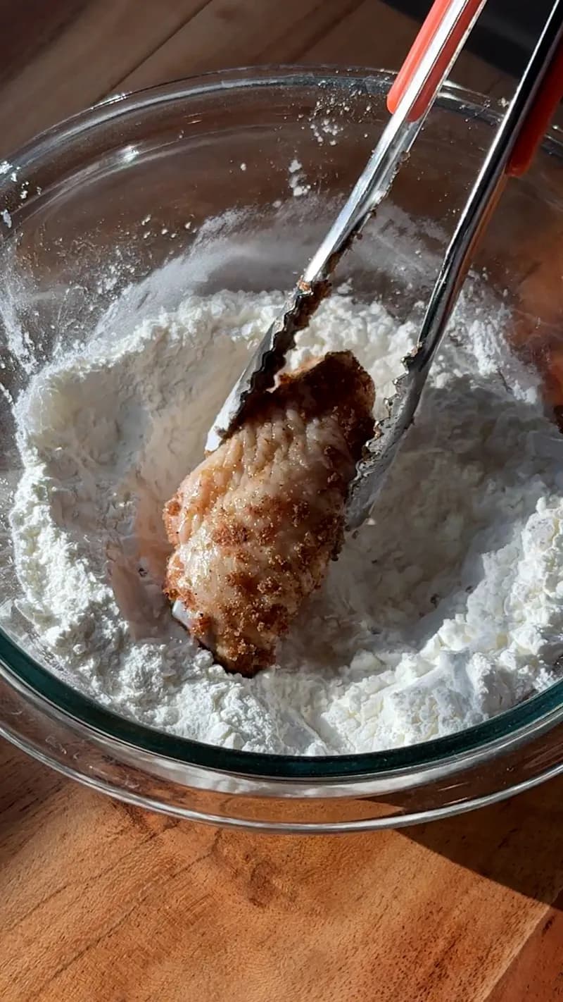 Seasoned chicken wing being coated in corn starch before air frying