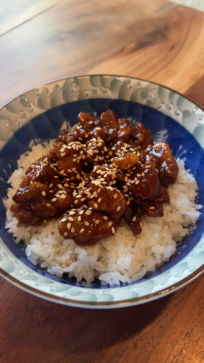 Spicy Korean chicken rice bowl — glossy gochujang-glazed chicken topped with sesame seeds over steamed white rice