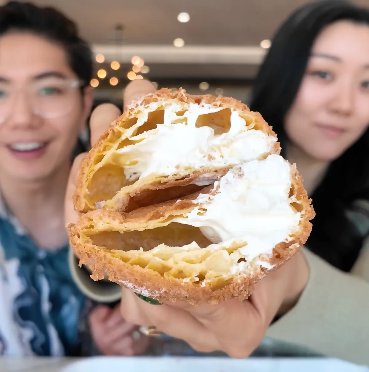 Jasmine and George holding an 85°C Bakery cream puff broken open showing the white cream filling inside