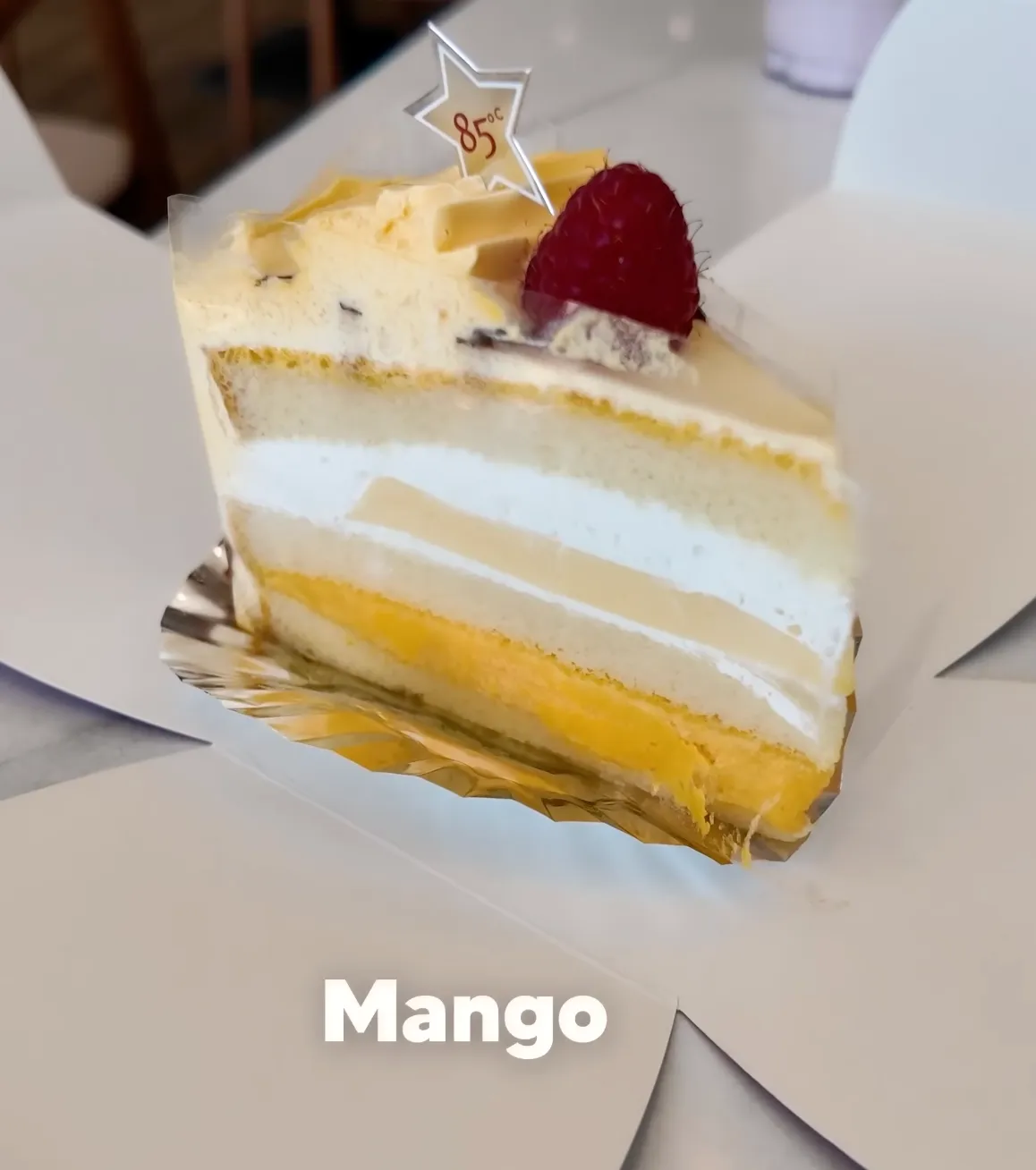 Slice of 85°C Bakery mango creme brulee cake showing layered mousse and mango filling with an 85°C star topper