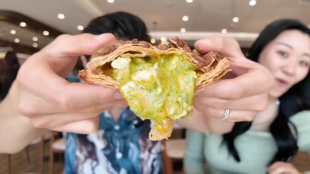Hands breaking open the pesto chicken hot sandwich revealing creamy green pesto filling inside flaky pastry