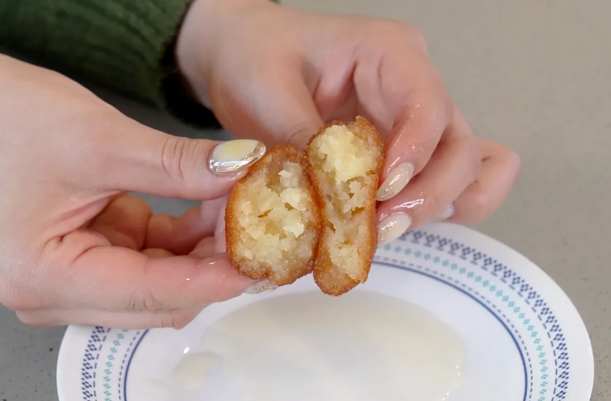 Hands breaking open a gulab jamun ball to show its soft fluffy interior above a white plate