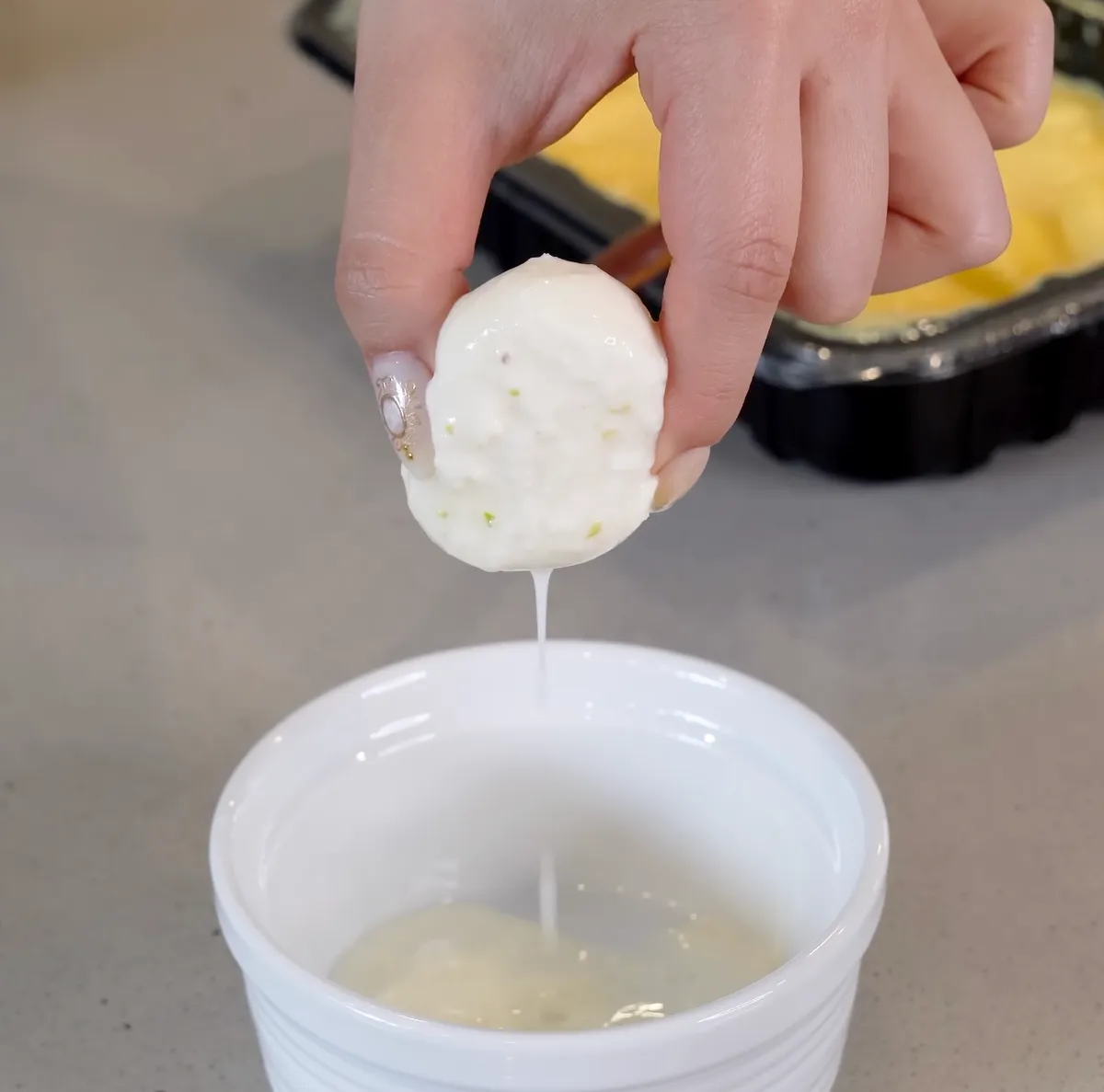 Hand squeezing a rasmalai disc over a white cup with cream dripping down