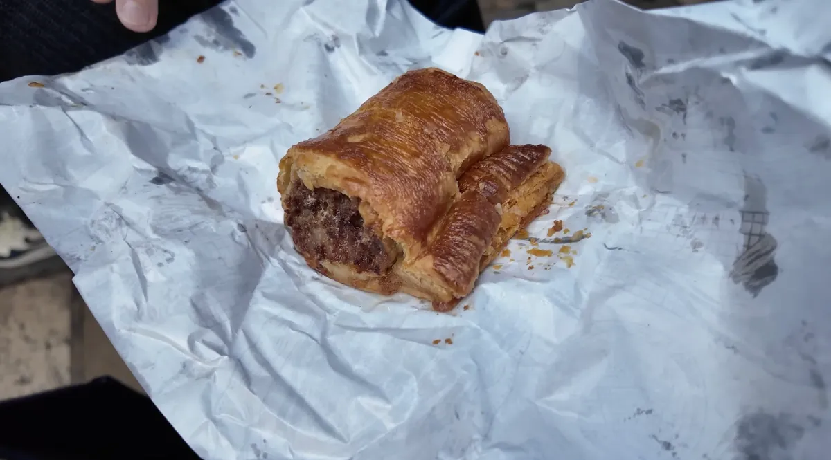 Ginger Pig sausage roll unwrapped in white paper at Borough Market London