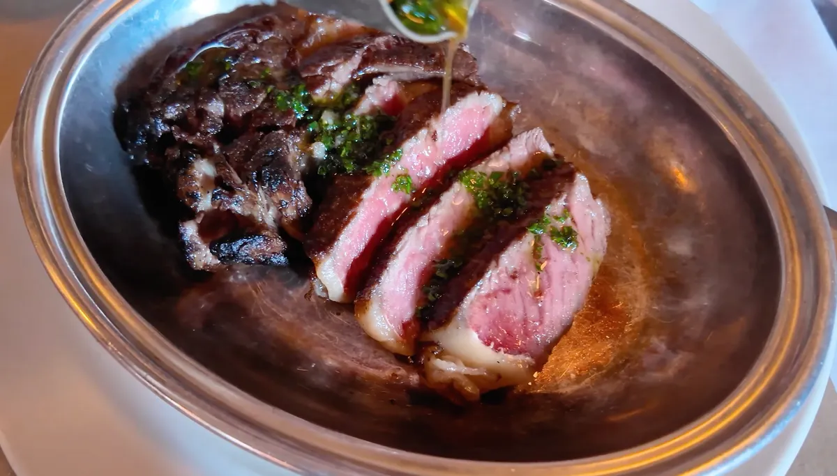 The Devonshire wood-fired ribeye sliced medium-rare in a silver dish with green herb sauce
