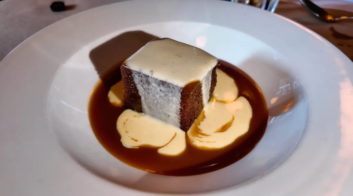 The Devonshire sticky toffee pudding with caramel sauce and custard on a white plate