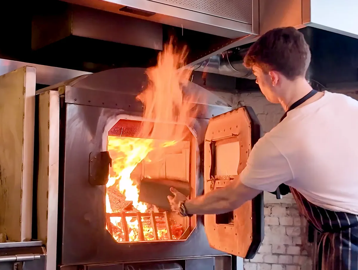 Chef at The Devonshire Soho loading wood-fired oven with open flames