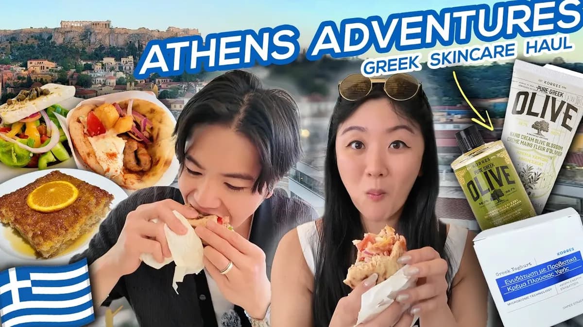 Jasmine and George smiling in front of the Athens Acropolis with Greek food spread in the foreground