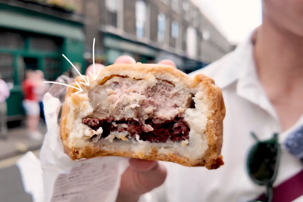George holding a Mrs. Kings pork and black pudding pie cross-section showing layers of meat and jelly on a London street