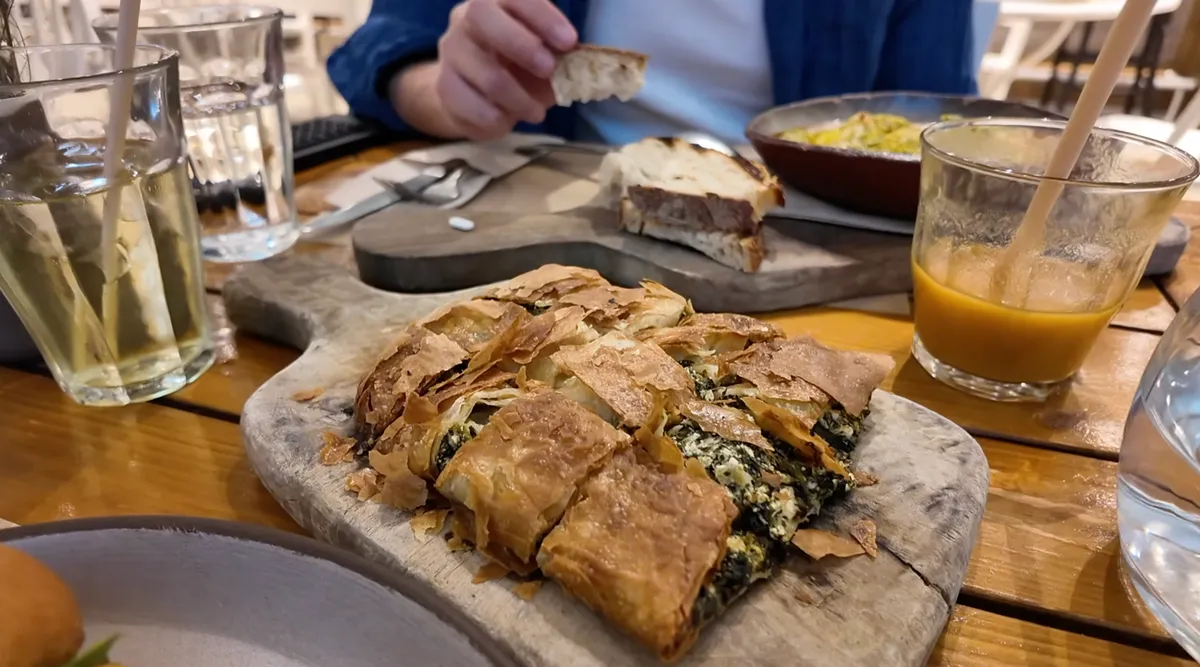 Crispy bougatsa cheese and spinach pie sliced on a wooden board at ERGON House Athens breakfast