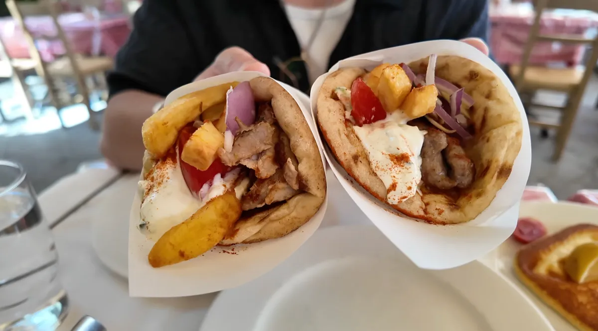 Pork and lamb kebab gyros held open to show the filling: fries, tomato, onion, tzatziki, and meat at O Thanasis Athens
