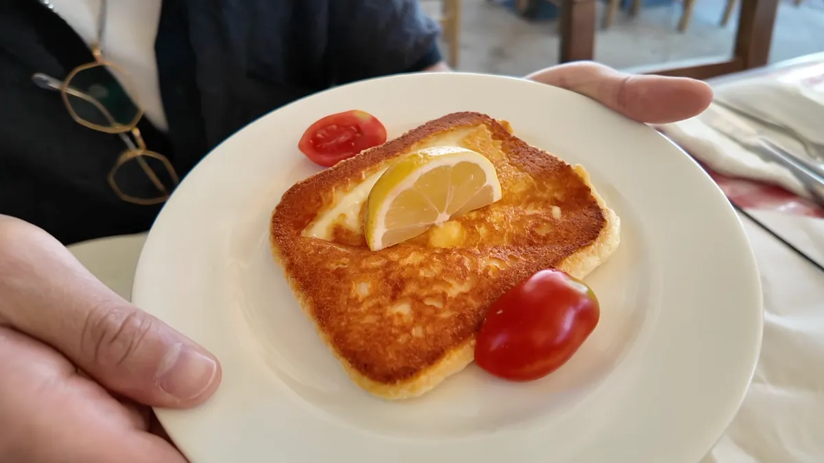 Grilled saganaki feta cheese on a white plate with lemon wedge and cherry tomatoes at O Thanasis Athens