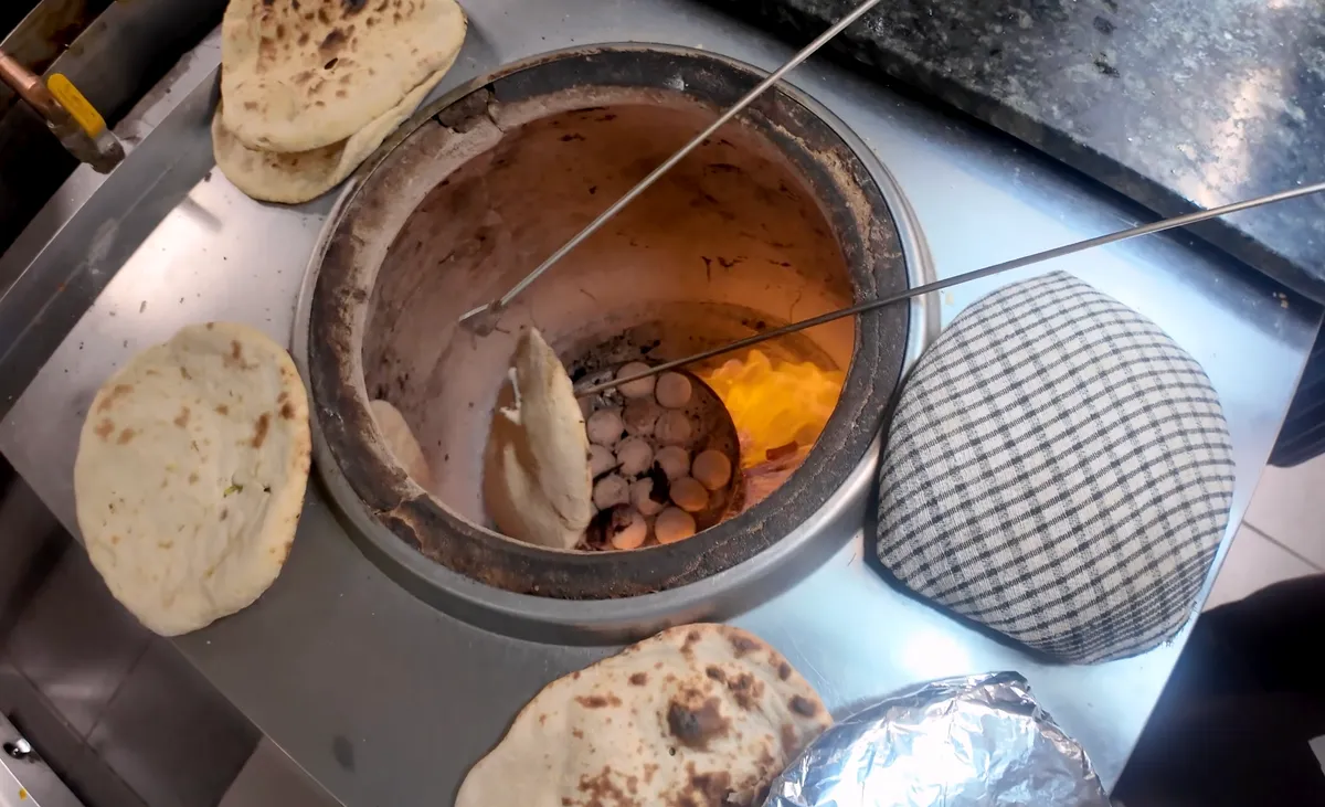 Inside view of a tandoor oven at Lahore Kebab Shop with naan breads resting on the rim and skewered meat cooking inside